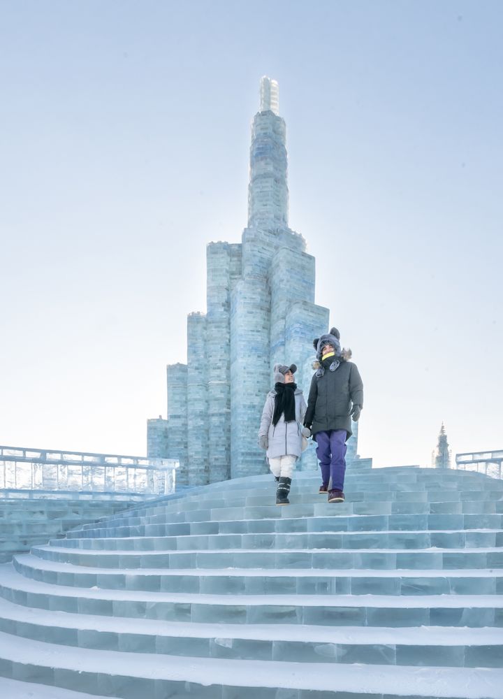 man and woman in warm outwear standing standing on illuminated castle of ice and snow