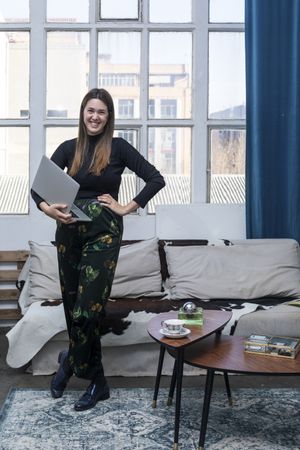 Smiling young female standing at home while holding a laptop