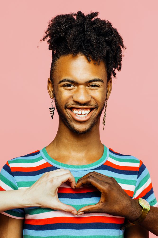 Portrait of a smiling man with earrings and heart shape with multiracial hands