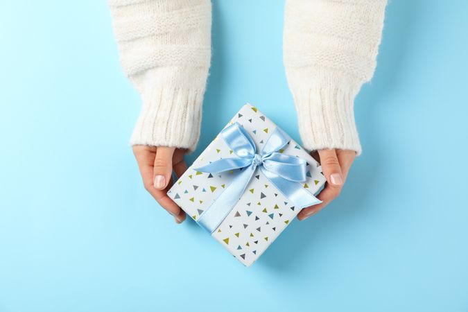 Young woman holding gift box on light blue background, space for text
