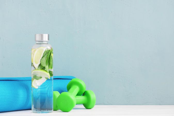 Dumbbells and fresh water with citrus and yoga mat on baby blue background