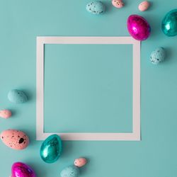 Easter composition made with colorful eggs on bright blue background with paper square outline