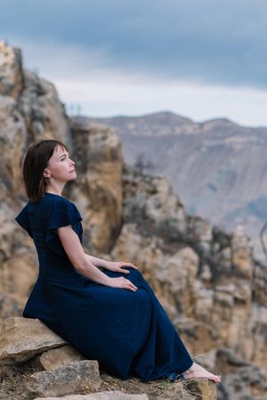 Side view of woman in blue dress sitting on brown rock