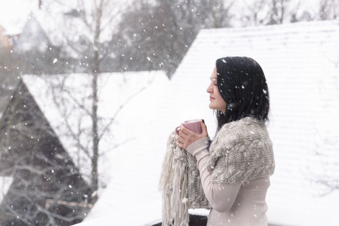 Woman with hot drink under snowfall