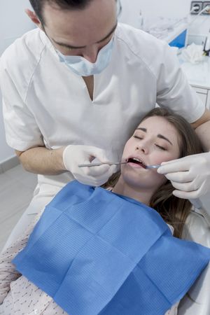 A portrait of a dentist working on the mouth of a female patient, vertical