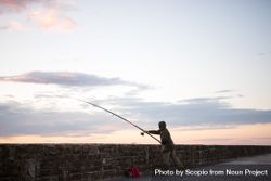 Person holding a fishing rod and standing on the beach during sunset 5axvG0