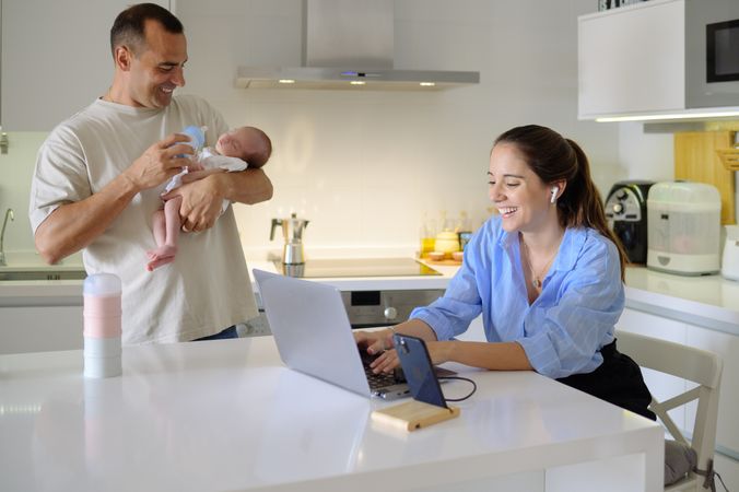 A man and woman holding a baby in front of a laptop
