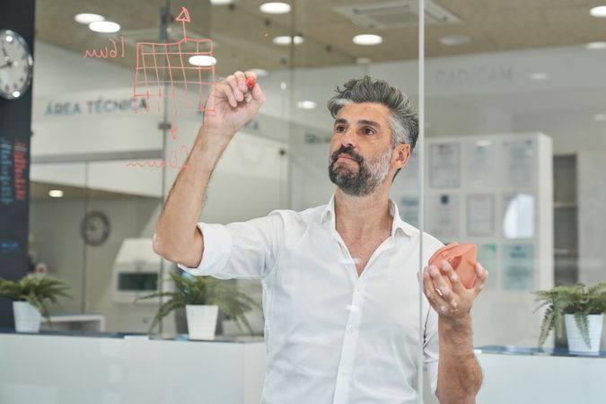 Focused man writing on glass while designing model of respirator
