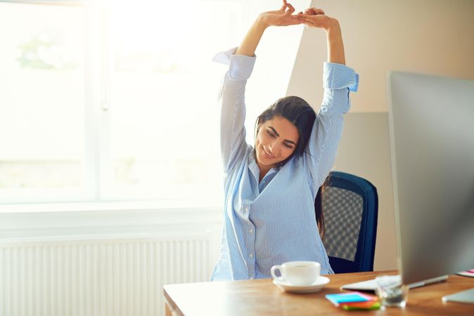 Smiling female sitting at her desk with her hands up in the air stretching