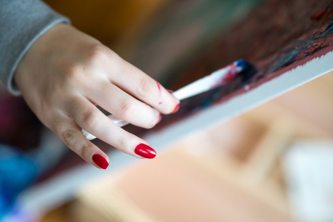 Woman with red nailpolish painting on canvas