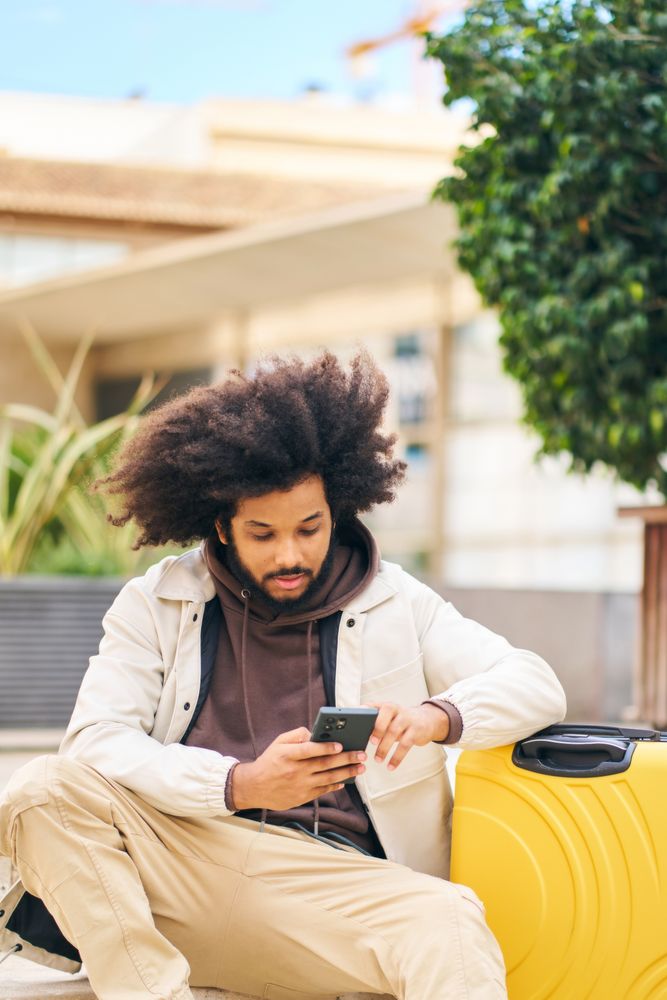 Young man with curly afro hair in the street watching social networks on mobile phone