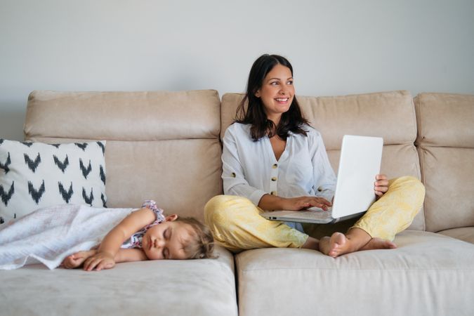 Happy mother working on laptop near sleeping daughter