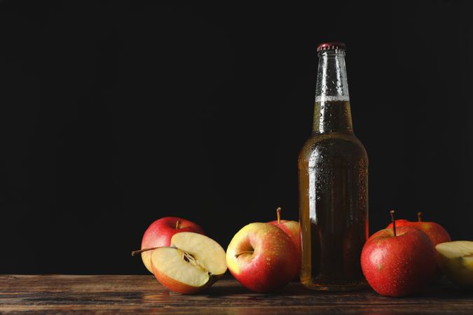 Composition with cider and apples on wooden table against dark background
