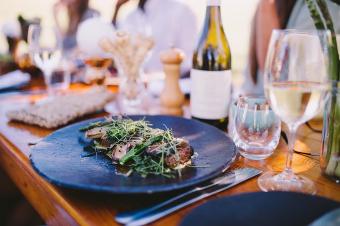Formal outdoor dinner setting with plated steak, greens and wine