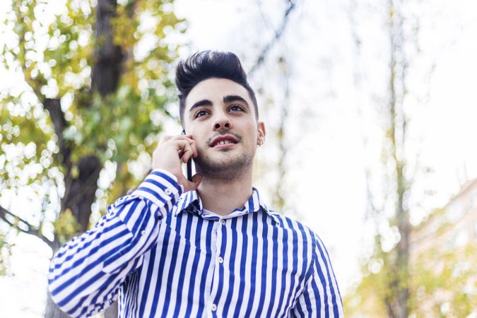Portrait of man standing in striped shirt speaking on phone outside