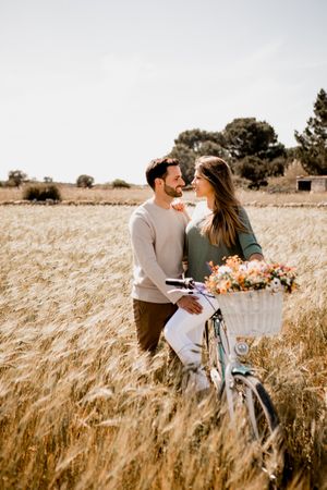 Sincere lovers posing by bicycle on rye field