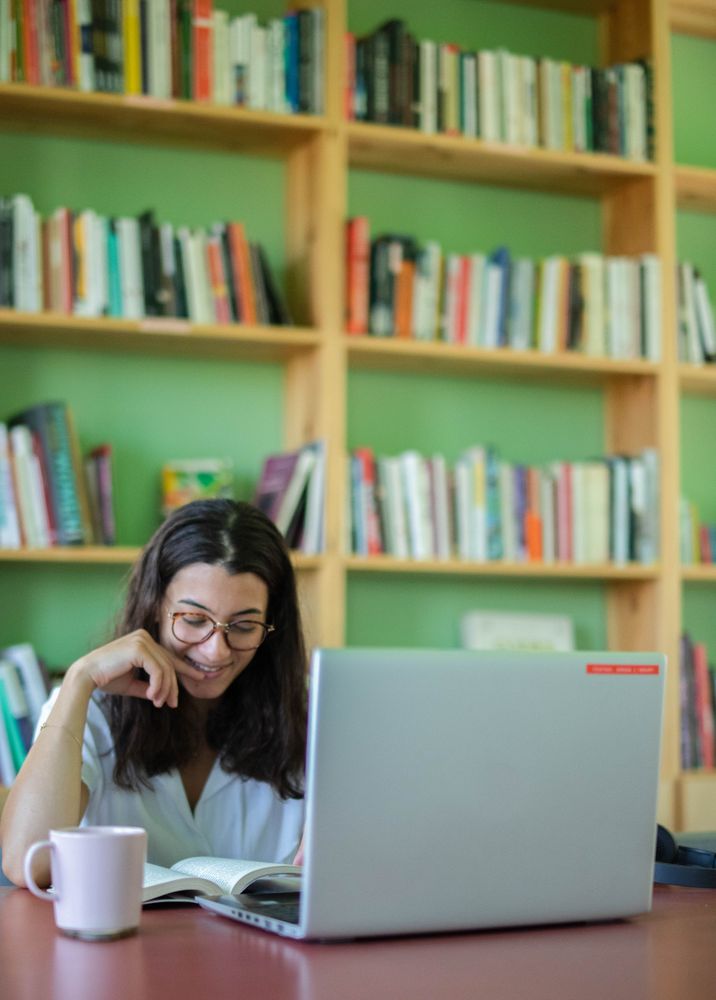 Woman smiling while reading a book and working on her laptop