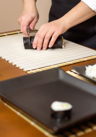 Closeup of woman chef cutting Japanese sushi rolls with rice, avocado and shrimps on nori seaweed sheet, vertical