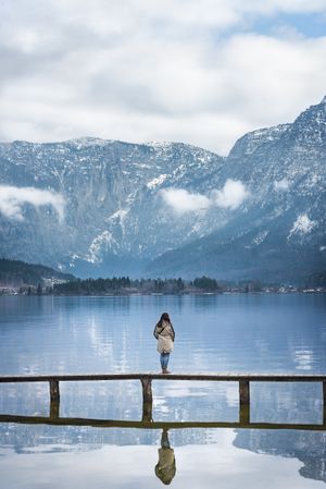 Woman standing on a bridge over a lake enjoying the scenery of the Alps mountains