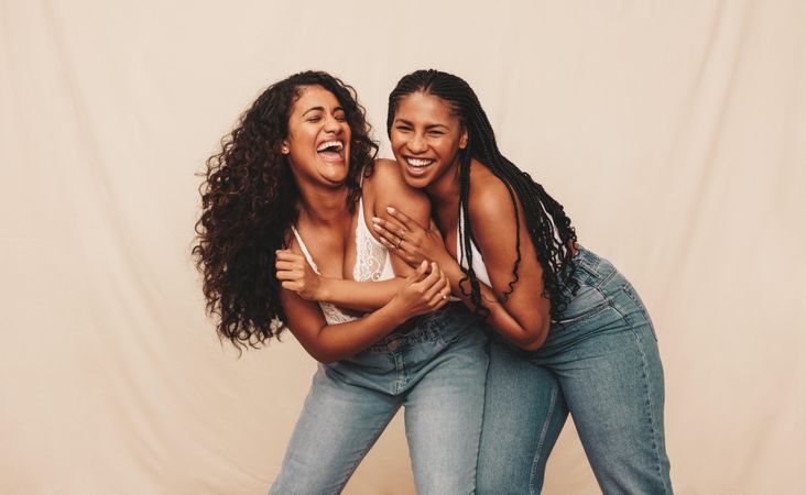 Two happy women laughing and being playful while wearing denim jeans against a studio background