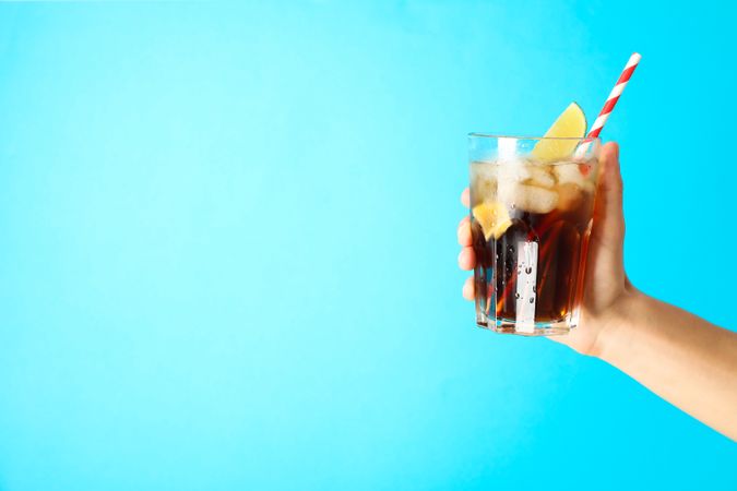 Female hand holding a glass with ice cola, tubule and lime slice