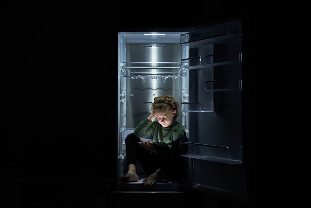 Focused kid watching movie on tablet while sitting in fridge