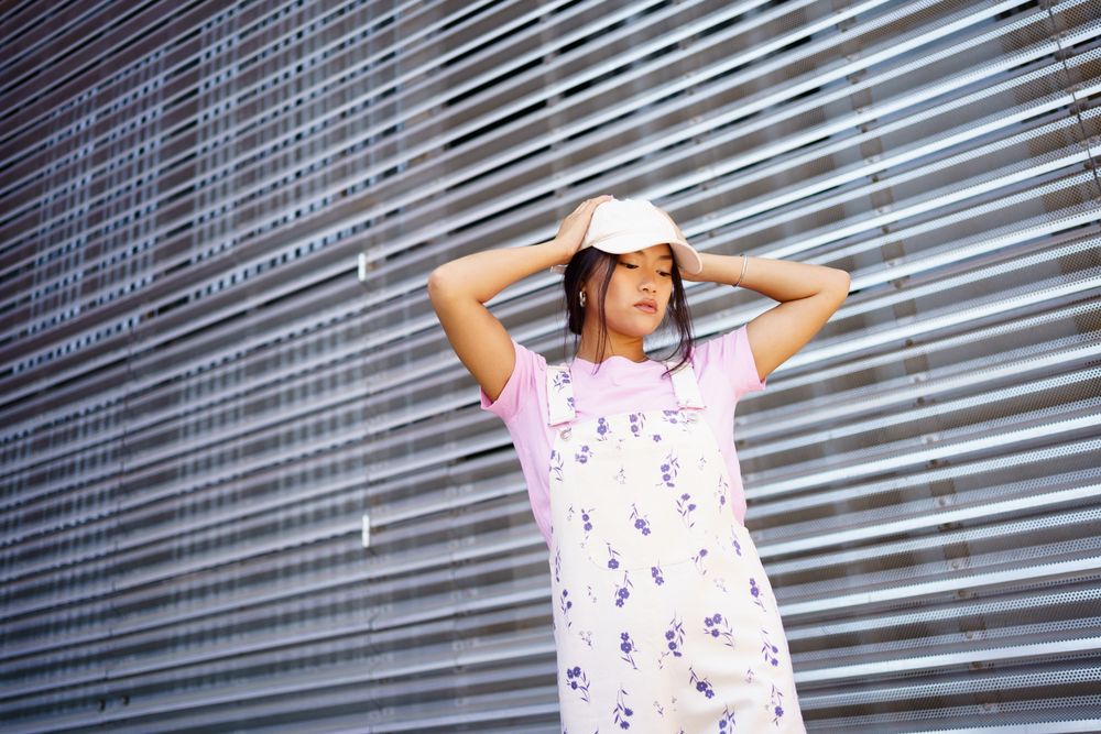 Chinese woman in floral coveralls holding her cap in front of metal wall