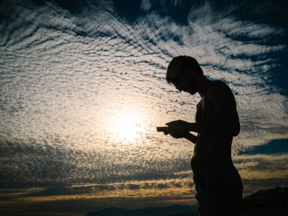 Man with smartphone against cloudy evening sky