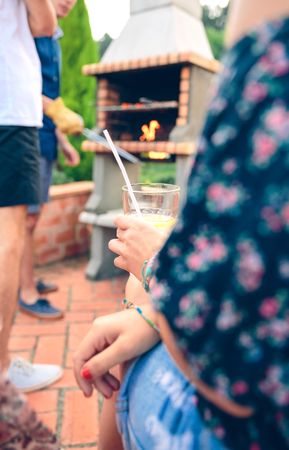 Woman holding lemonade glass and friends cook on a barbecue