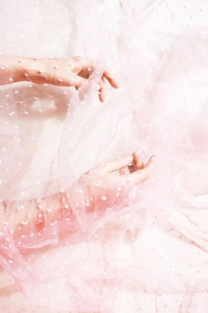 Elegant female hands under pink transparent light fabric