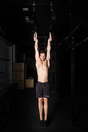 Man hanging on gymnastic rings between darkness in gym