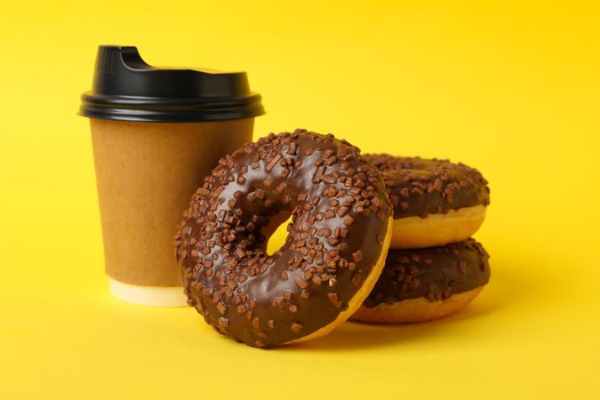 Paper cup and tasty donuts on yellow background