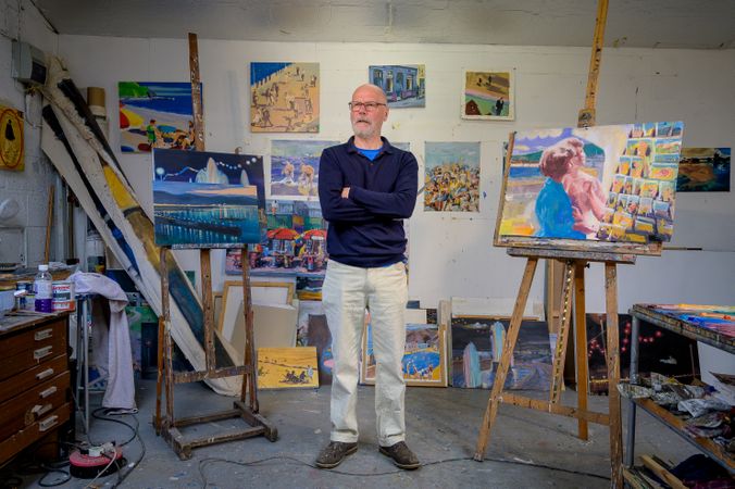 Proud male with arms crossed surrounded by paintings in art studio