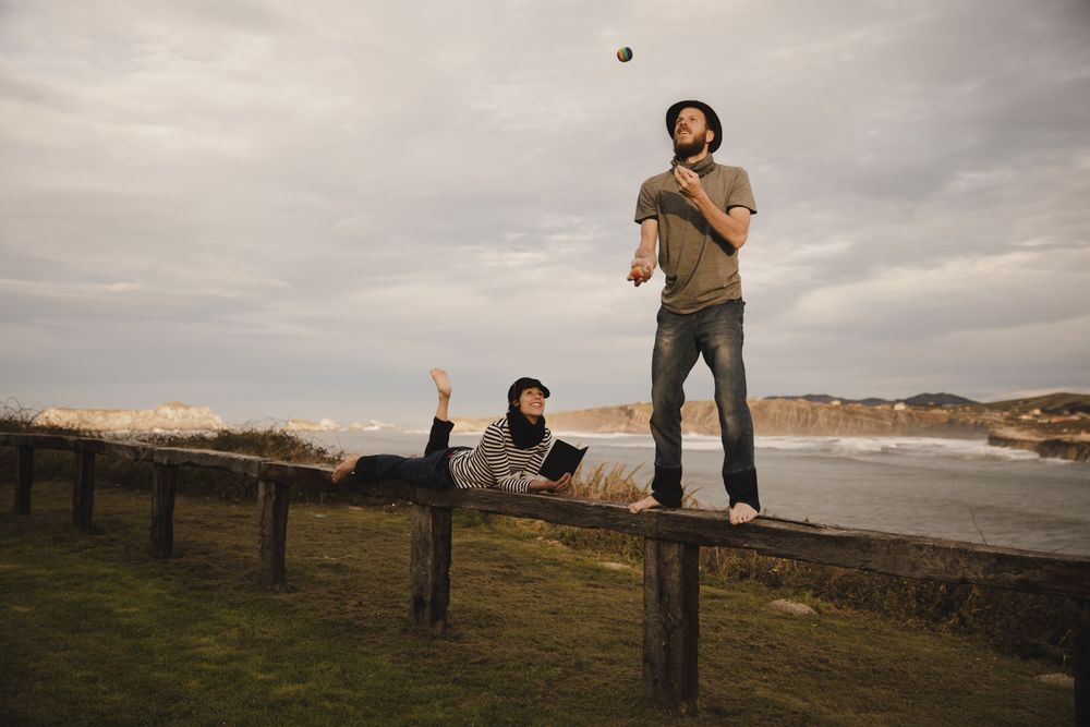 Man juggling balls on bench near woman with drum on shore