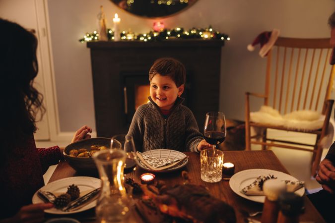 Boy sitting in front of fireplace having Christmas dinner with family