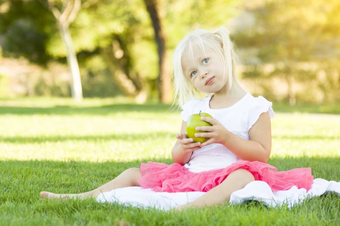 Little Girl In Grass Eating Healthy Apple