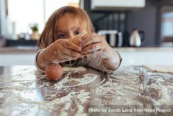 Little girl breaking an egg on kitchen counter covered with flour 42Mx75