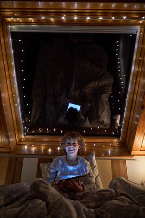 Cheerful boy browsing tablet in dark bedroom