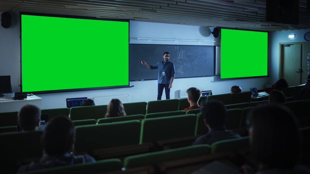 Young Male Teacher Giving a Lecture, Showing Slides on a Green Screen Mock Up