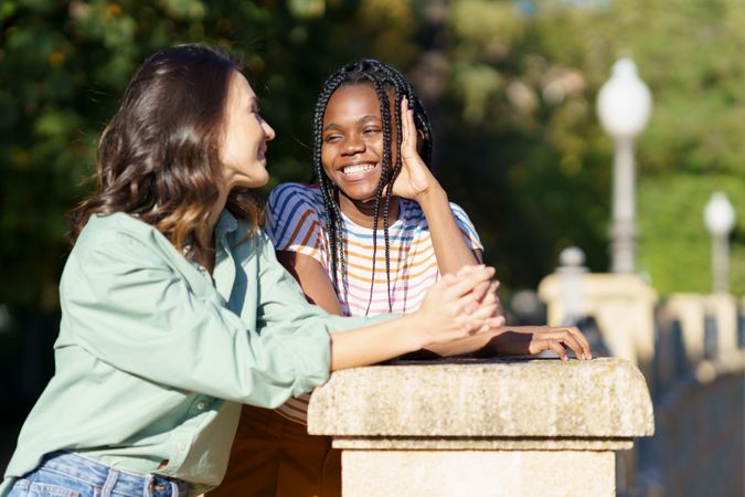 Female friends leaning on wall in casual clothing outside