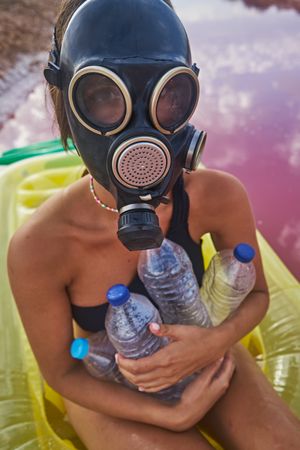 Female in gas mask and with plastic bottles in lake water