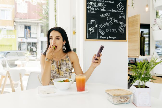 Cheerful woman with healthy food talking on smartphone in cafe