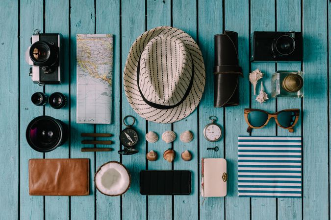 Mix of travel items; hat, camera, map, compass, seashells, arranged on blue background