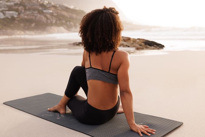 Female stretching her back twisting her spine while sitting next to the ocean