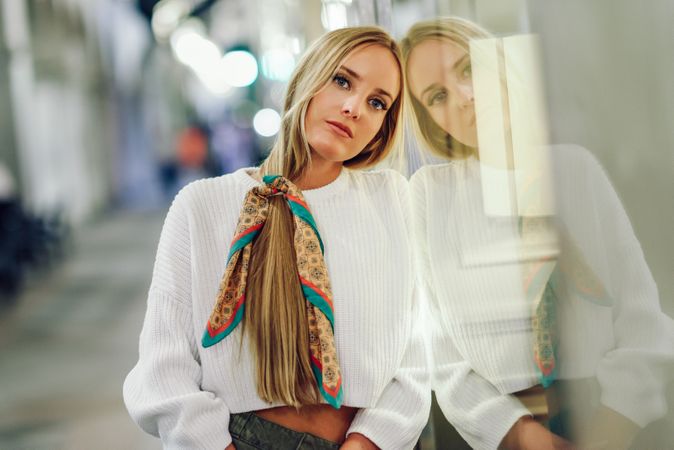 Chic woman with scarf in hair leaning on glass of shop outside