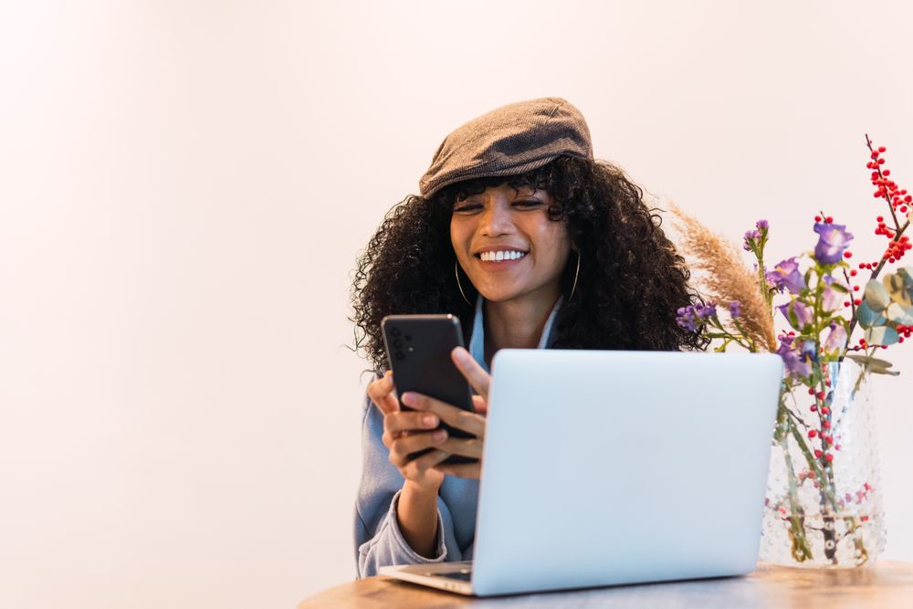 Cheerful Black woman using smartphone and laptop