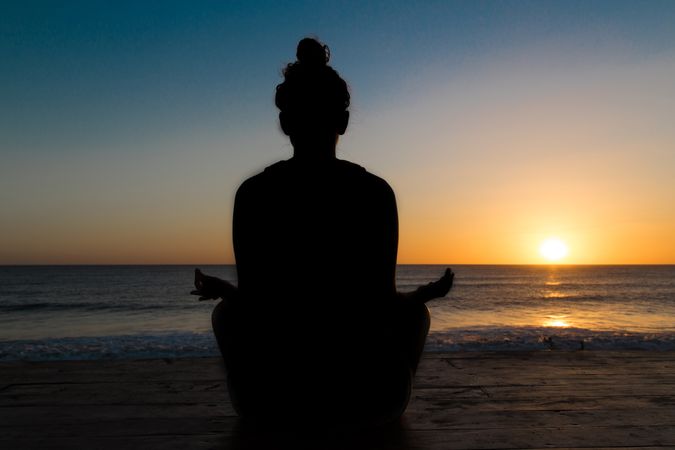 Woman meditating on seashore at sunset