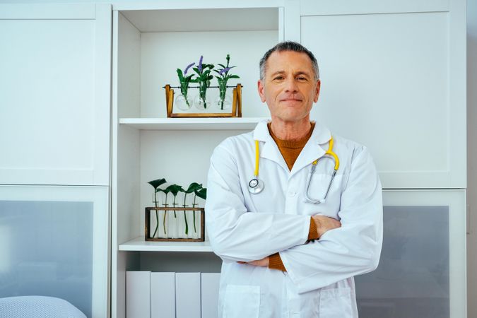 Older male doctor standing in his office with arms crossed