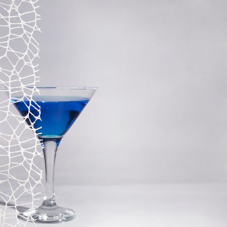 Blue cocktail in martini glass behind lace