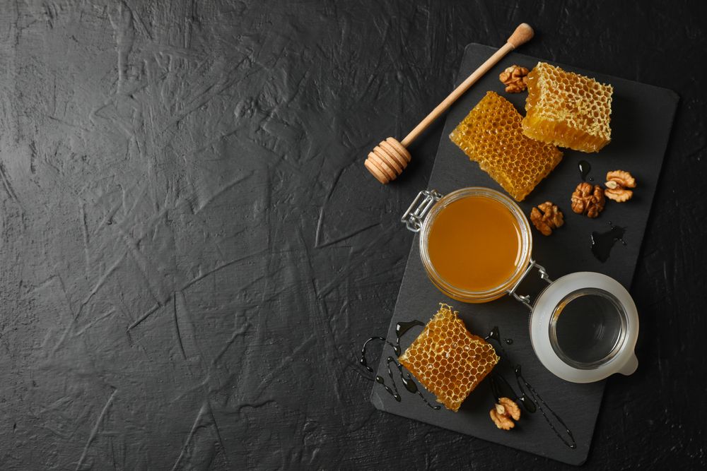 Walnut, honeycombs, jar with honey and dipper on dark background, copy space